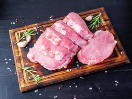 bife de porco, filé de carbonato cru em fundo escuro, carne com alecrim, temperos, vista lateral