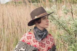 jovem viajante com poncho e chapéu caminhando nos campos e na fazenda foto