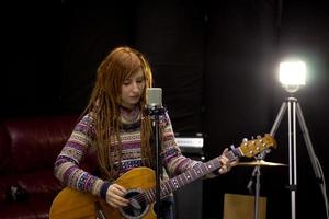 jovem mulher com guitarra canta no estúdio foto