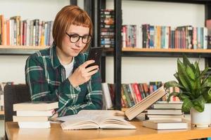 mulher jovem ruiva de óculos ler livro na biblioteca foto