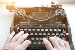dedos digitam no teclado de uma velha máquina de escrever mecânica em estilo retrô, à luz do sol.
