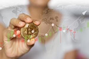 mão segurando a imagem da moeda bitcoin com fundo de gráfico de comércio golbal. foto