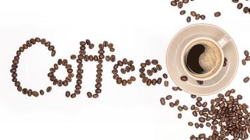 xícara de café e grãos de café espalhados com fonte a palavra feita de grãos de café isolados em um fundo branco foto