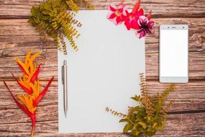 espaço conceitual para texto, que consiste em papel em branco, azaléia, flores de manjericão, telefones celulares e caneta em um fundo de madeira. foto