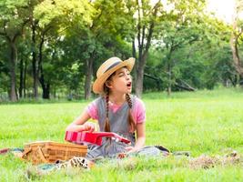 a menina senta-se na grama e aprende a tocar ukulele, aprendendo fora da escola no parque natural foto