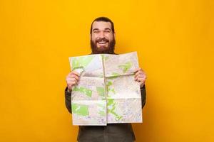 homem barbudo animado está segurando um mapa de papel enquanto sorri para a câmera.