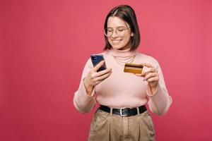 mulher sorridente está usando mobile banking enquanto segura seu telefone e um cartão. foto