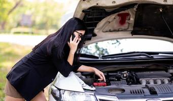 uma jovem asiática está chamando seu técnico de serviço para consertar um carro quebrado na beira da estrada foto