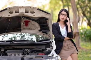 uma jovem asiática está chamando seu técnico de serviço para consertar um carro quebrado na beira da estrada foto