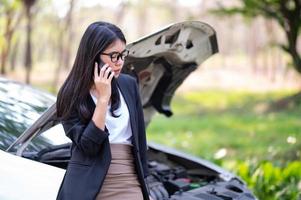 uma jovem asiática está chamando seu técnico de serviço para consertar um carro quebrado na beira da estrada foto