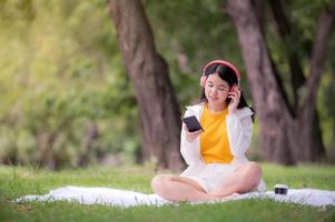 linda mulher asiática relaxando no jardim e usando um telefone celular, pode pesquisar música ou fazer compras online na internet foto