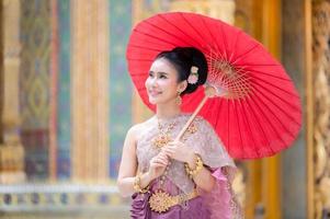 uma linda e graciosa mulher tailandesa em vestido tailandês adornado com joias valiosas segurando guarda-chuva vermelho foto