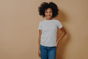 alegre fêmea africana em camiseta branca e jeans expressando emoções positivas, posando no estúdio foto