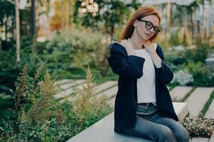 foto ao ar livre da mulher ruiva tem poses de dor no ombro ao ar livre no parque durante o dia