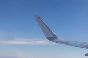 asa de avião com belo horizonte do nascer do sol. avião voando no céu azul. vista da janela do avião. voo comercial da companhia aérea pela manhã com luz solar. asa de avião acima das nuvens. foto