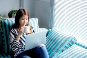 linda de retrato jovem asiática sentada use cartão de crédito com laptop e beba café, garota de conteúdo compras on-line e pagamento com notebook no sofá, conceito de estilo de vida.