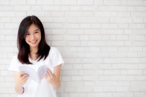 linda de retrato jovem mulher asiática felicidade relaxe em pé lendo livro sobre fundo branco de cimento concreto em casa, menina feliz estudo conteúdo literatura, educação e conceito de estilo de vida. foto