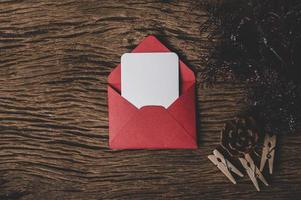 um cartão em branco com um envelope vermelho e um prendedor de roupa colocado no fundo de madeira foto