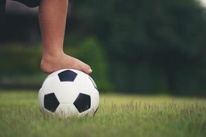 pés de menino segurando futebol no campo de grama foto