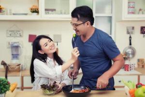 casal feliz comendo vegetais. se divertindo na cozinha. foto