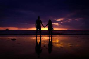 silhueta de casal se abraçam e feliz casal jovem ama na praia na hora do pôr do sol foto