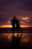 silhueta de casal se abraçam e feliz casal jovem ama na praia na hora do pôr do sol foto