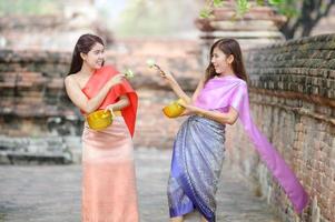 senhora tailandesa atraente em vestido tradicional tailandês segurando flores de lótus brincando com amigos no festival tailandês songkran foto