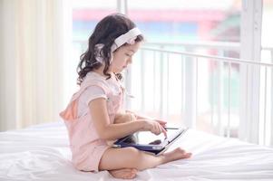 uma linda garota asiática está usando um tablet para se divertir jogando e aprendendo na sala foto