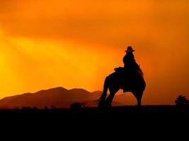 o vaqueiro ocidental forçou seus cavalos a parar enquanto o sol estava se pondo, em terras onde a lei ainda não chegou foto