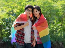 casais homossexuais asiáticos usam uma bandeira lgbt para cobrir e dar as mãos no amor foto