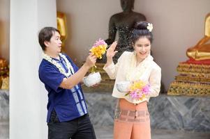 homens e mulheres tailandeses jovens em vestido tailandês tradicional seguram flores espirrando água para se divertir no festival de água songkran