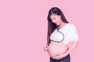 mulheres asiáticas grávidas usam um estetoscópio para tocar sua barriga para ouvir seu bebê ainda não nascido foto