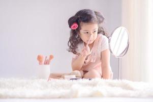 uma menina asiática bonitinha está alegremente aplicando pincéis de maquiagem com pó em seu quarto foto