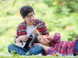 casais femininos asiáticos lgbt sentados e tocando ukulele no jardim e se abraçam com amor e felicidade foto