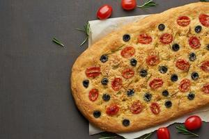 focaccia, pizza, pão italiano com tomate, azeitonas e alecrim na mesa marrom, copie o espaço