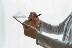 mulher segurando o tablet e escrevendo nele, pessoa com vista lateral do dispositivo closeup foto