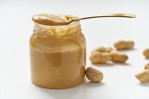 pote de manteiga de amendoim e amendoim com casca em uma mesa branca, vista lateral, nozes moídas frescas, vista lateral foto