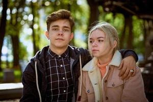 adolescentes apaixonados sentam-se no banco do parque, descansando em raios de sol de outono, menino olhando para a frente. conceito de amor adolescente foto