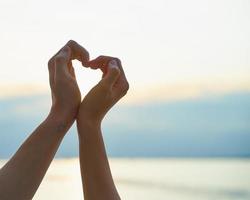 mão feminina e masculina mostrando coração, símbolo de amor, fundo de praia foto