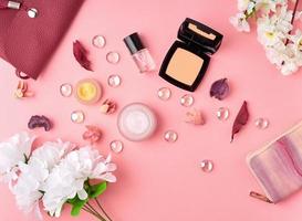 acessórios de mulher plana leiga com cosméticos, creme facial, bolsa, flores na mesa rosa brilhante. foto