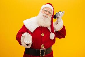 papai noel com celular em fundo amarelo. conceito de comunicação, empresas de telefonia e promoções. foto