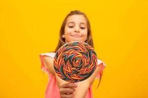 a criança está segurando um pirulito. alegria infantil é doçura. menina em fundo amarelo. foto