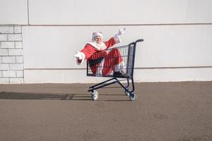 carrinho de supermercado com papai noel dentro. braços abertos. compras para o conceito de natal. foto