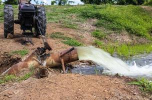 a água corre de tubos de aço para campos de arroz verde e veículos agrícolas. foto