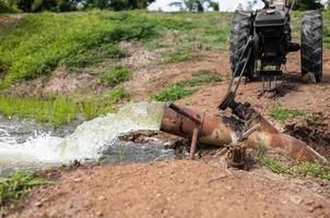 a água corre de tubos de aço para campos de arroz verde e veículos agrícolas. foto