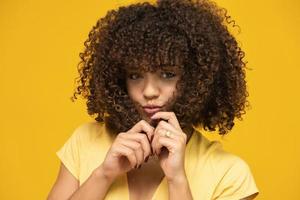 feliz rindo americana mulher com seu cabelo encaracolado em fundo amarelo. rindo mulher encaracolada na camisola tocando seu cabelo e olhando para a câmera. foto