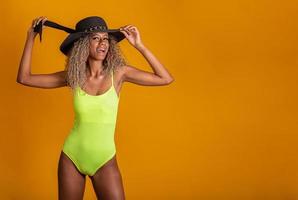 garota atraente de cabelo encaracolado em um maiô de praia verde brilhante, chapéu, boca emocionalmente aberta em um fundo amarelo brilhante com um corpo perfeito. isolado. tiro de estúdio. foto
