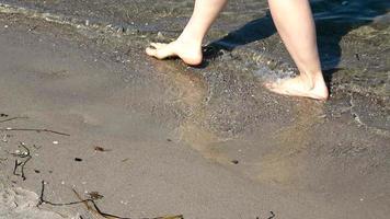 pés femininos jovens andando na água rasa em uma praia do mar Báltico no verão foto