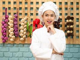 mulher asiática com uniforme de chef está cozinhando na cozinha. cozinheiro feminino retrato sorrindo com espaço de cópia. foto