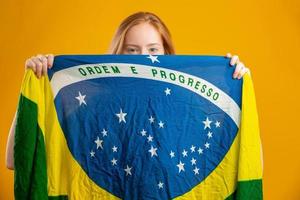 fã de mulher ruiva misteriosa segurando uma bandeira brasileira na sua cara. cores do brasil em fundo, verde, azul e amarelo. eleições, futebol ou política. foto